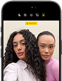 iPhone 18 Pro, kolor czarny, przód obudowy, na ekranie widoczne dwie osoby pozujące do zdjęcia, prezentacja aparatu przedniego Center Stage